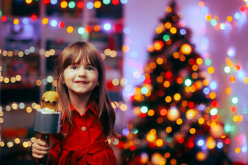 Happy Girl Holding a Microphone Singing Carols. Cheerful child performing Christmas songs for her family at home
