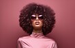 Black woman with large afro and chic sunglasses against a pink backdrop, epitomizing cool and modern style.