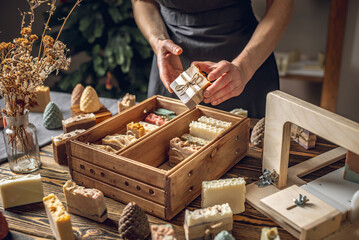 Wall Mural - A woman soap maker holds handmade soap in her hands. A lot of different sliced pieces in a wooden box. Eco-friendly natural handmade cosmetics