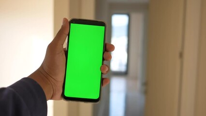 close-up hand using phone showing green screen in empty room