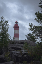 Red And White Lighthouse On A Rock Between Green Trees