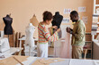 © Seventyfour - Two young African American couturiers with piece of fatin standing by mannequin while one of them pinning fabric during work