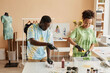 © Seventyfour - Young craftsman and craftswoman in protective gloves tie dying crumpled cotton t-shirts together while binding clothes and applying paint