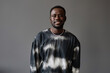 Happy young male fashion model wearing tie dye pullover looking at camera with smile while posing in isolation over grey background