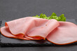 meat product. sliced juicy pink ham with green lettuce leaves on a charcoal black board on a gray wall background