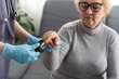 © Angelov - Medical help at home. Woman doctor in a medical mask measures the patient's pulse and oxygen saturation to middle aged woman using a pulse oximeter while sitting on sofa, healthcare concept.