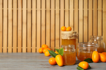 Sticker - Kumquat and jars of jam on wooden background, space for text