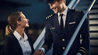Male pilot and a female flight attendant are smiling and having a conversation on the tarmac, with a commercial airplane in the background.