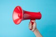 powerful of hand gripping a red megaphone on blue background, conveying messages with authority, amplified communication, and impactful announcements.