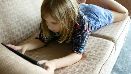 the girl plays on the tablet in online games lying on the couch.