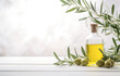 Bottle olive oil and olive branches on white wooden table over light kitchen background