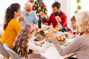 Family holding hands and praying before Christmas dinner at home