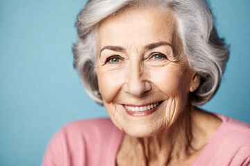 Wall Mural - Happy beautiful elderly senior model with grey hair in a pink t-shirt on a blue background, portrait of beauty mature old woman with hairstyle and makeup, healthy face skin with wrinkles, dental care