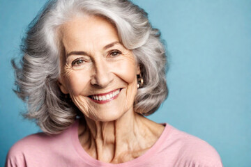 Happy beautiful elderly senior model with grey hair in a pink t-shirt on a blue background, portrait of beauty mature old woman with hairstyle and makeup, healthy face skin with wrinkles, dental care