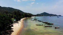 A Pedestal Aerial Drone Shot Of Sairee Beach Showing A Number Of Fishing Boats, Some Fishermen, And Tourists At The Beachfront Located In Koh Tao Island In Surat Thani Province, Thailand.