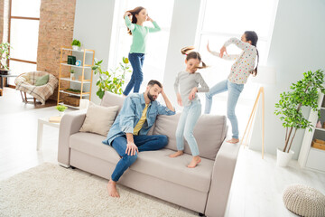 Wall Mural - Portrait of four persons thoughtful man sit on sofa hand on head carefree girls standing have fun dancing indoors