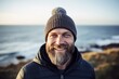 Portrait of a grinning man in his 40s donning a warm wool beanie against a serene seaside background. AI Generation