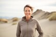 Portrait of a grinning woman in her 40s wearing a thermal fleece pullover against a serene dune landscape background. AI Generation