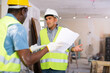 African-american foreman quarreling with his employee, caucasian man, about project documentation. Conflict of two men builders in construction site.