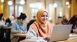 A young Asian student in a hijab smiles while working on a laptop in the library.