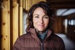 © CogniLens - Portrait of a smiling woman in her 40s donning a durable down jacket against a scandinavian-style interior background. AI Generation