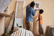 © Seventyfour - Back view of young man and his son handing painting on wall together while decorating spacious living room of their new apartment