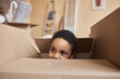 Face of cute little boy peeking out of big cardboard box and looking aside while playing and hiding from his parents during relocation