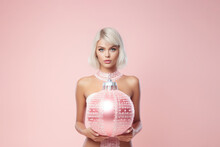 Portrait Of A Beautiful Girl With Decorative Christmas Bauble In Her Hands On Pink Backround. Minimal Style. AI Generated
