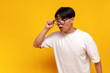 © Богдан Маліцький - young shocked asian guy in glasses looks surprised at copy space on yellow isolated background