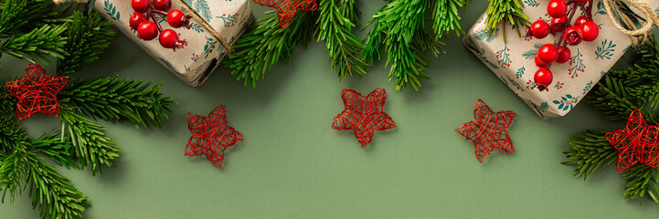 Wall Mural - Christmas festive banner, fir branches and gift boxes with a sprig of rowan and red stars on a green background, top view