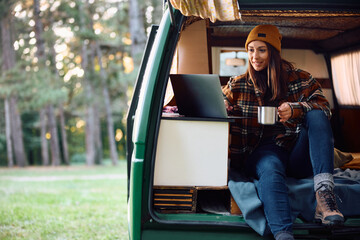 Happy woman surfing the net on laptop in camper van.