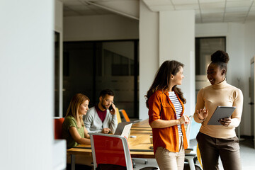 Wall Mural - Two young business women with digital tablet in the office in front of their team