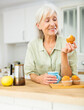 Portrait of relaxed elderly woman drinking coffee with muffing at kitchen