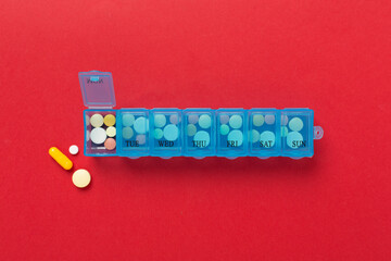 Daily pill organizer with medications on color background, top view