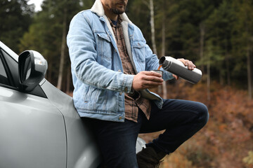 Poster - Man pouring hot drink from metallic thermos into cup lid near car, closeup