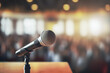 Close up of microphone on the table in background of blurred a conference seminar audience and conference hall. Event concept of classes and speeches.
