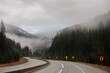 © Liudmila - Asphalt road in the middle of high mountains, covered with fog and clouds, at dusk. American winter landscape of a mountainous area covered with fir forest