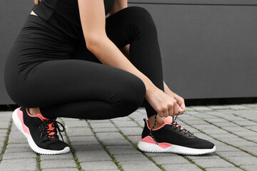 Poster - Woman tying shoelace of sneakers on street, closeup