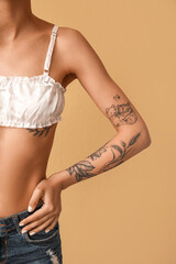 Wall Mural - Young woman with tattooed arm on beige background, closeup