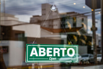 Bilingual sign with the words Aberto and Open in Portuguese and English on the glass door of a store in Brazil