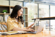 © ArLawKa - Ambitious Asian girl working from home Looking at laptop screen and financial documents, woman is checking email or doing research while working remotely.