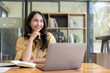 © ArLawKa - Ambitious Asian girl working from home Looking at laptop screen and financial documents, woman is checking email or doing research while working remotely.