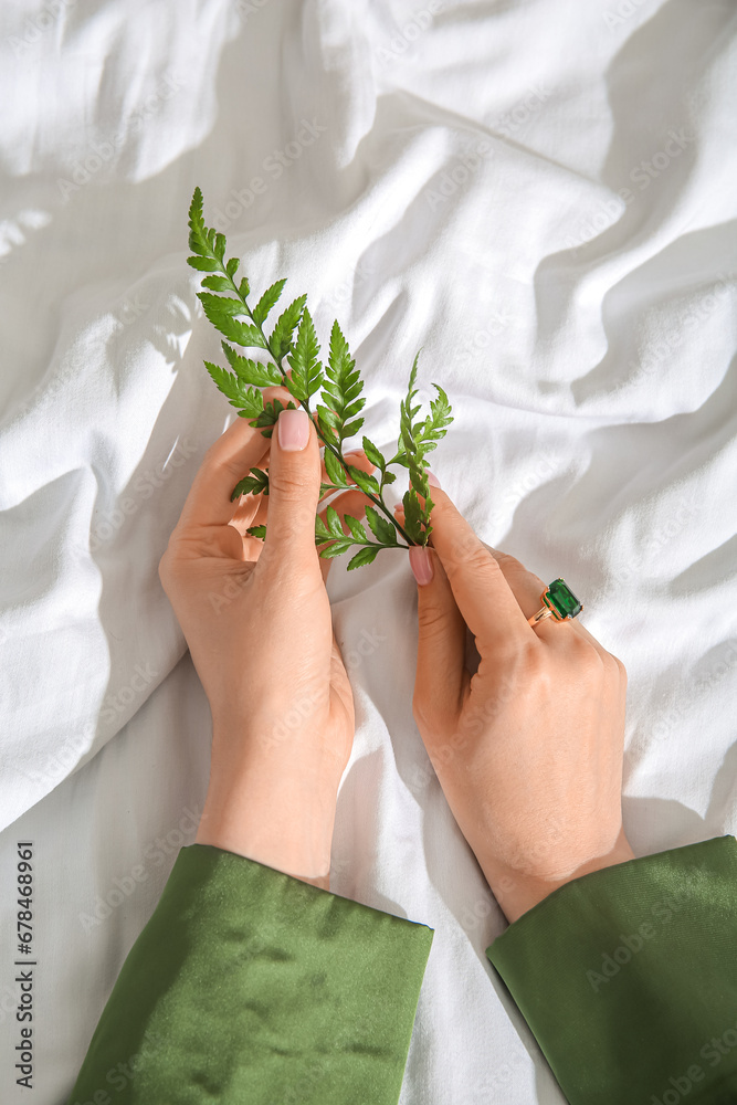 Female hands with beautiful emerald ring and plant branch on white cloth