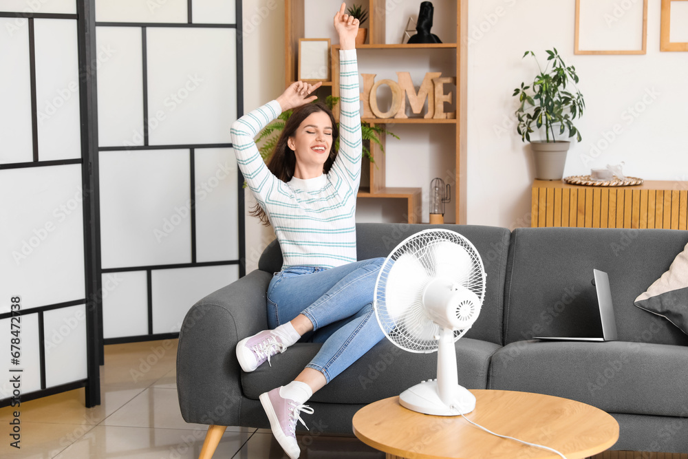 Young woman with blowing electric fan at home