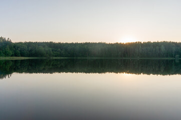 Wall Mural - Lake surrounded by trees that reflect in the water. Fog on the surface of the forest