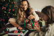 © polinaloves - Young beautiful mother and her daughter packing and wrapping presents in a cozy decorated bedroom with Christmas tree.