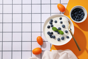 Wall Mural - Bowls with yogurt and berries, spoon and towel on white and yellow background, space for text