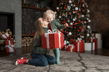 Mother with little daughter with Xmas presents by christmas tree in living room traditional New Year decorated living room.