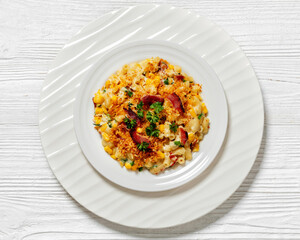 Wall Mural - portion of mac and cheese with corn, bacon topped with panko breadcrumbs on white plate on white wooden table, horizontal view from above, flat lay, close-up