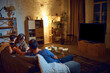 © master1305 - Back view of parents and children spending evening together, sitting on couch in living room and watching tv, eating snacks. Concept of family, leisure time, relaxation, childhood and parenthood